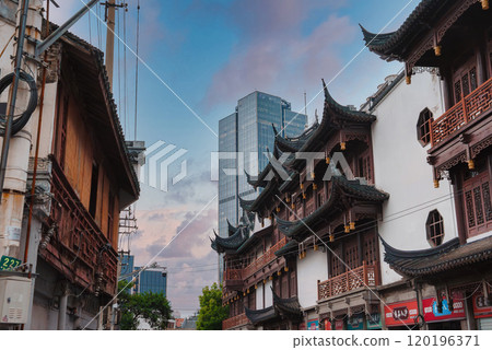 A vibrant Shanghai street scene contrasts traditional Chinese buildings with a modern skyscraper. The sky is a soft blue with hints of pink. 120196371