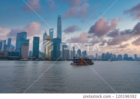 View of Shanghai's Pudong district skyline, featuring Shanghai Tower, World Financial Center, and Jin Mao Tower. A traditional boat cruises the Huangpu River. 120196382
