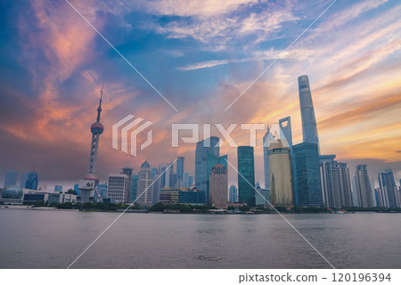 The iconic skyline of Shanghai features the Oriental Pearl Tower and Shanghai Tower against a vibrant sky. The Huangpu River reflects the modern architecture. 120196394