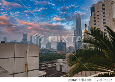 View of Shanghai's skyline featuring the Shanghai World Financial Center, modern skyscrapers, and traditional architecture. Lush greenery and a palm tree in the foreground under a vibrant sunset sky. View of Shanghai's skyline featuring the Shanghai World Financial Center, modern skyscrapers, and traditional architecture. Lush greenery and a palm tree in the foreground under a vibrant sunset sky. 120196446