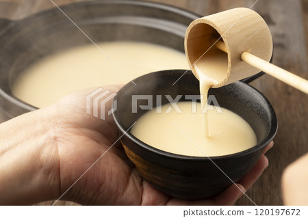 Amazake: Pour warm amazake with a ladle into a teacup held in the hand. 120197672