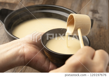 甘酒 用長柄湯匙將溫熱的甘酒倒入手中的茶杯中 甘酒 用長柄湯匙將溫熱的甘酒倒入手中的茶杯中 120197676