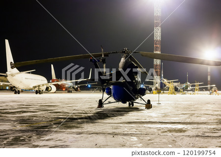 Rear view of the helicopter and passenger airplanes on the airport apron at winter night 120199754