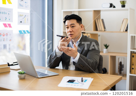 Asian businessman recording audio message in modern office setting Asian businessman recording audio message in modern office setting 120201516