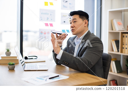 Asian businessman recording audio message in modern office setting 120201518