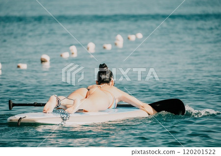 Sea woman sup. Silhouette of happy middle aged tanned woman in rainbow bikini, surfing on SUP board, confident paddling through water surface. Idyllic sunset. Active lifestyle at sea or river. Sea woman sup. Silhouette of happy middle aged tanned woman in rainbow bikini, surfing on SUP board, confident paddling through water surface. Idyllic sunset. Active lifestyle at sea or river. 120201522