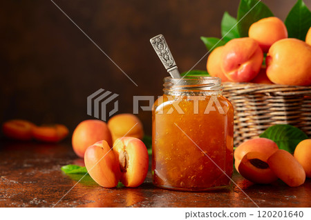 Apricot jam in glass jar and fresh fruits on a brown table. Apricot jam in glass jar and fresh fruits on a brown table. 120201640