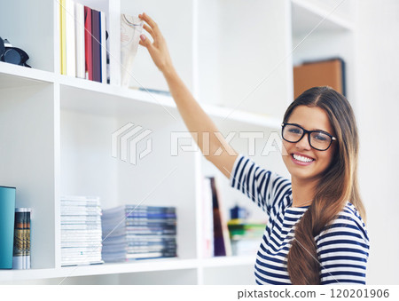 Just the book I was looking for. Portrait of a smiling young woman reaching for a book on a shelf at home. Just the book I was looking for. Portrait of a smiling young woman reaching for a book on a shelf at home. 120201906