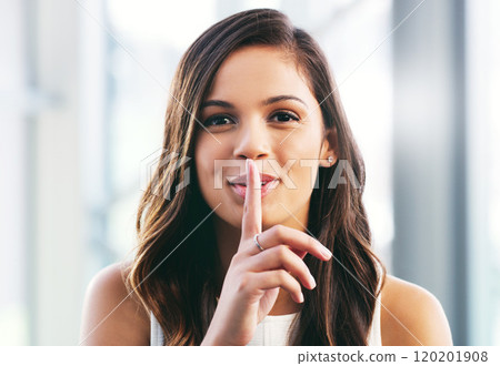 Dont tell anyone, but...Portrait of a young businesswoman placing her finger on her lips in a modern office. Dont tell anyone, but...Portrait of a young businesswoman placing her finger on her lips in a modern office. 120201908