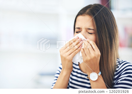 Its that time of the year again. Shot of a young woman with allergies sneezing into a tissue at home. 120201926