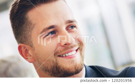 He isnt fully dressed without his smile. Cropped shot of a handsome young businessman smiling while looking away in the office during the day. 120201956