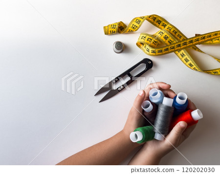 Childrens hands holding colorful thread spools with sewing tools on white background 120202030