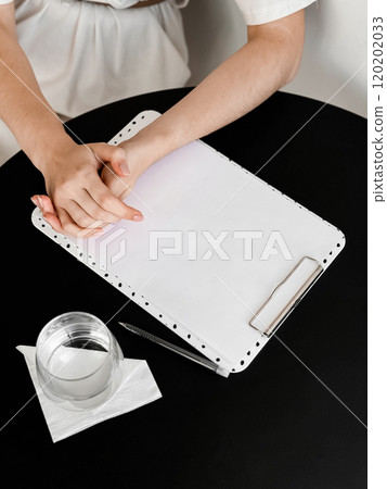 Professional hands on clipboard with glass of water and pen on black table 120202033