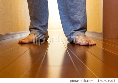 A barefoot person standing on a wooden corridor 120203901