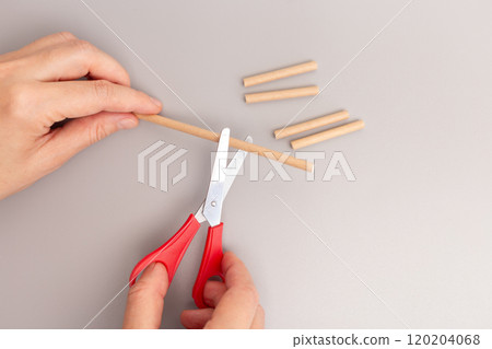 Close up of hand holding scissors cutting paper straw step in creative process DIY quick assembly simplified children toy, 120204068