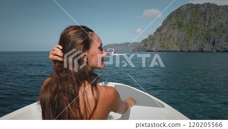 Young woman is enjoying a boat trip in the tropics, touching her hair and admiring the scenic view of a green rocky island Young woman is enjoying a boat trip in the tropics, touching her hair and admiring the scenic view of a green rocky island 120205566