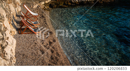 Three beach chairs along the tranquil pebbled shore by crystal-clear water, inviting relaxation. 120206833