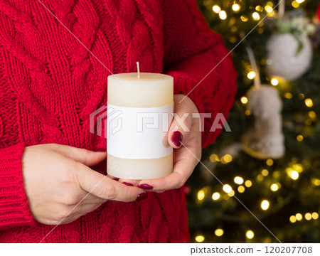 Woman in red sweater with pillar candle in hands against Christmas tree lights, mock up 120207708
