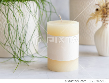 Pillar candle with blank label on marble near potted green plant close up, mockup Pillar candle with blank label on marble near potted green plant close up, mockup 120207719