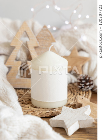 Pillar candle with label near white sweater and wooden Christmas decor and lights, mockup Pillar candle with label near white sweater and wooden Christmas decor and lights, mockup 120207723