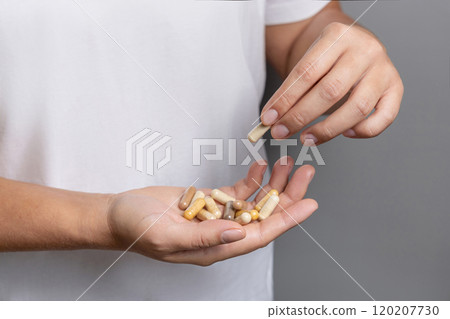Woman holding in hands beige medical herbal capsules closeup over white shirt 120207730