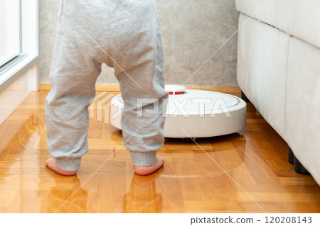 A curious baby exploring the robot vacuum cleaner in a modern home. A curious baby exploring the robot vacuum cleaner in a modern home. 120208143