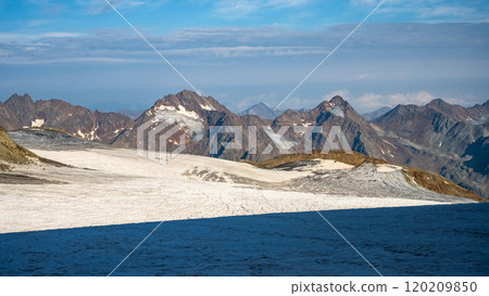 The Taschachferner Glacier in the Otztal Alps displays its icy surface under a clear sky, framed by rugged mountain peaks, creating a stunning landscape. 120209850