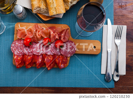Spanish tasty meal slicing sausages and ham with tomatoes at wooden desk Spanish tasty meal slicing sausages and ham with tomatoes at wooden desk 120210230