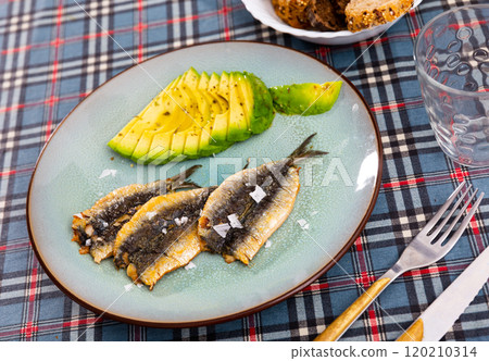 Smoked fillet of sardine carcass is served in plate with slices of ripe avocado. Smoked fillet of sardine carcass is served in plate with slices of ripe avocado. 120210314