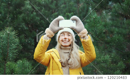 Happy smiling woman taking selfie with smartphone in winter park against Christmas tree, using phone Happy smiling woman taking selfie with smartphone in winter park against Christmas tree, using phone 120210483