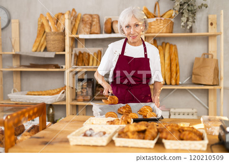Mature saleswoman putting croissants in wicker basket in bakery Mature saleswoman putting croissants in wicker basket in bakery 120210509
