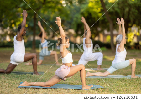 Girl performing Anjaneyasana during group yoga outdoors 120210631