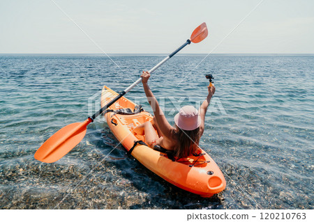 Kayaking Woman Paddle Sea - A woman wearing a pink hat paddles a bright orange kayak in a clear blue sea. Kayaking Woman Paddle Sea - A woman wearing a pink hat paddles a bright orange kayak in a clear blue sea. 120210763