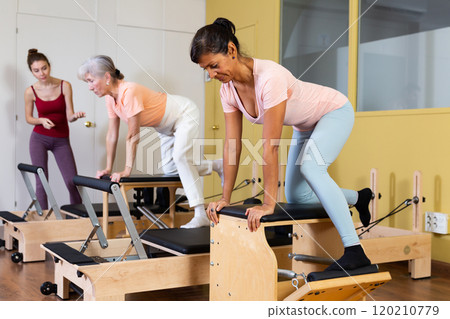 Hispanic woman practicing pilates stretching exercises on combo chair Hispanic woman practicing pilates stretching exercises on combo chair 120210779