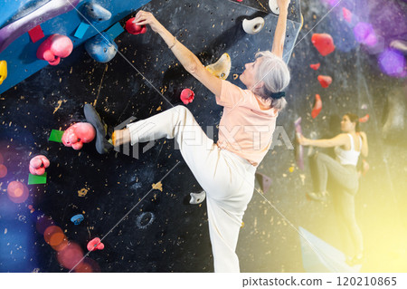 Mature female fitness climber training at bouldering gym.Woman rise up on artificial climbing wall Mature female fitness climber training at bouldering gym.Woman rise up on artificial climbing wall 120210865