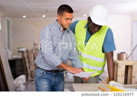 Owner of cottage discusses with worker drawings of room being repaired 120210977