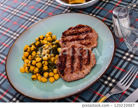 Barbequed cutlet is complemented with stewed chickpeas and spinach. Barbequed cutlet is complemented with stewed chickpeas and spinach. 120210987