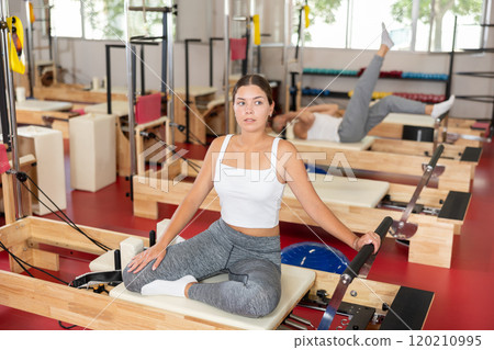 Active young woman doing arm exercises on reformer device 120210995