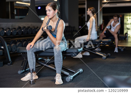Slender girl trains muscles of arms and back using dumb-bell shaped figure weighting. 120210999