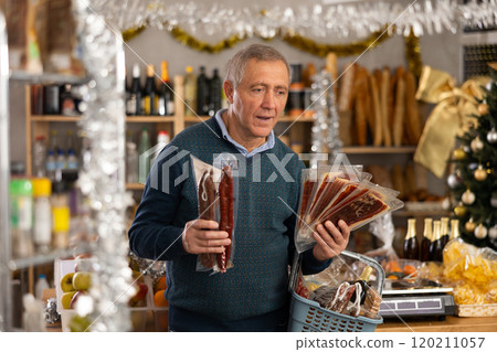Mature man with a basket of groceries buys dried sausage and ham in supermarket 120211057