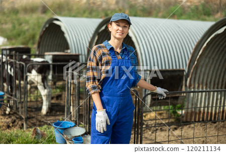 Portrait of female farmerwith bucket against the background of calf pen on summer day Portrait of female farmerwith bucket against the background of calf pen on summer day 120211134