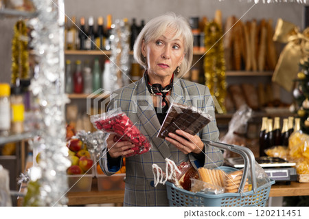 Elderly woman chooses chocolates and candies in grocery 120211451