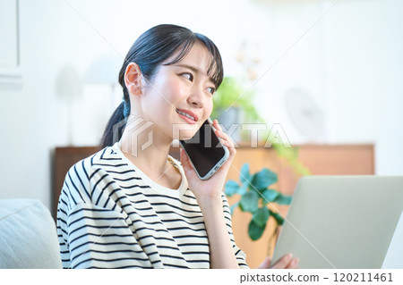 Young woman making a phone call in the living room, living room, one-room apartment Young woman making a phone call in the living room, living room, one-room apartment 120211461