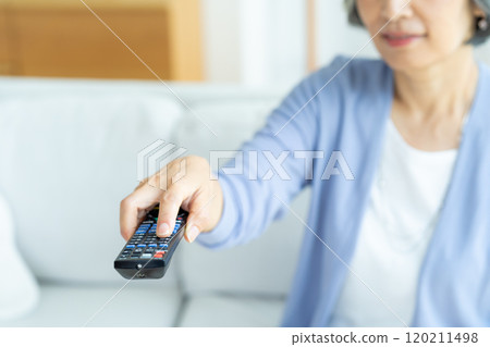 Senior woman operating a TV remote control in the living room Senior woman operating a TV remote control in the living room 120211498