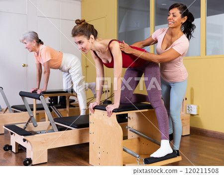Young woman practicing pilates on wunda chair with Hispanic female trainer 120211508