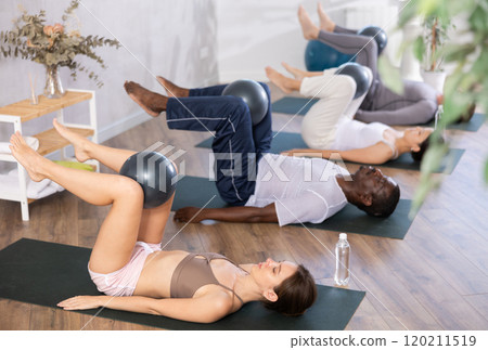 Young woman doing exercises with pilates ball during group workout Young woman doing exercises with pilates ball during group workout 120211519