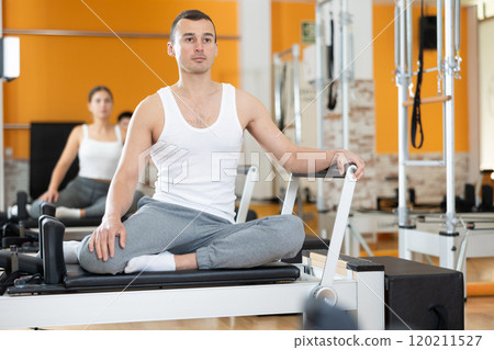 Man sits on reformer and rests while doing exercises for muscles of body and torso. Man sits on reformer and rests while doing exercises for muscles of body and torso. 120211527