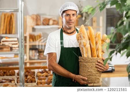 Portrait of experienced male baker with basket of fresh baguettes in bakery interior Portrait of experienced male baker with basket of fresh baguettes in bakery interior 120211581