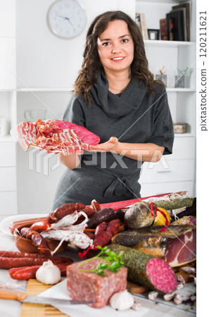 Woman costs near table on which sausages and smoked meat Woman costs near table on which sausages and smoked meat 120211621