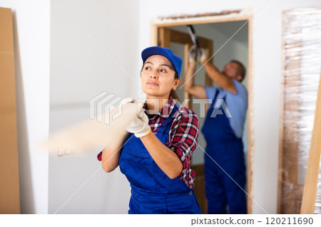 Positive Latin female carpenter in uniform holding wooden planks indoors 120211690